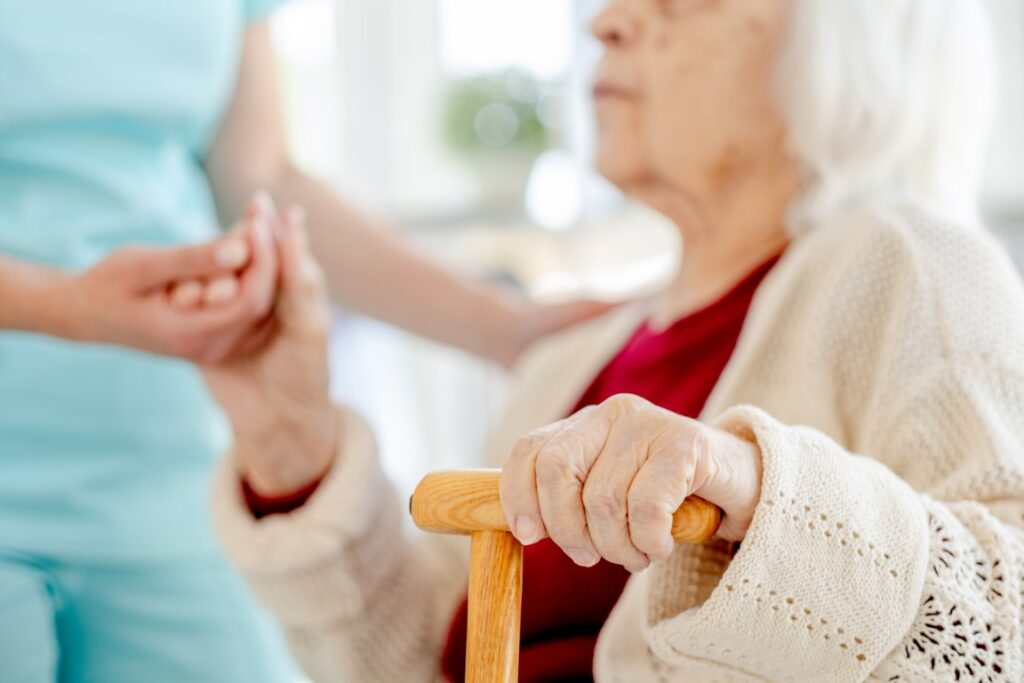 Close Up Of Nurse'S Hand Holding Elderly Woman'S Hand With Cane