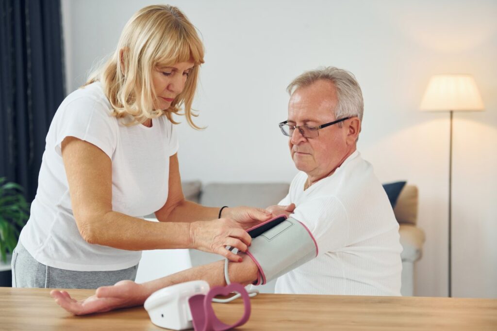 Wife measuring blood preasure her husband senior man woman is together home